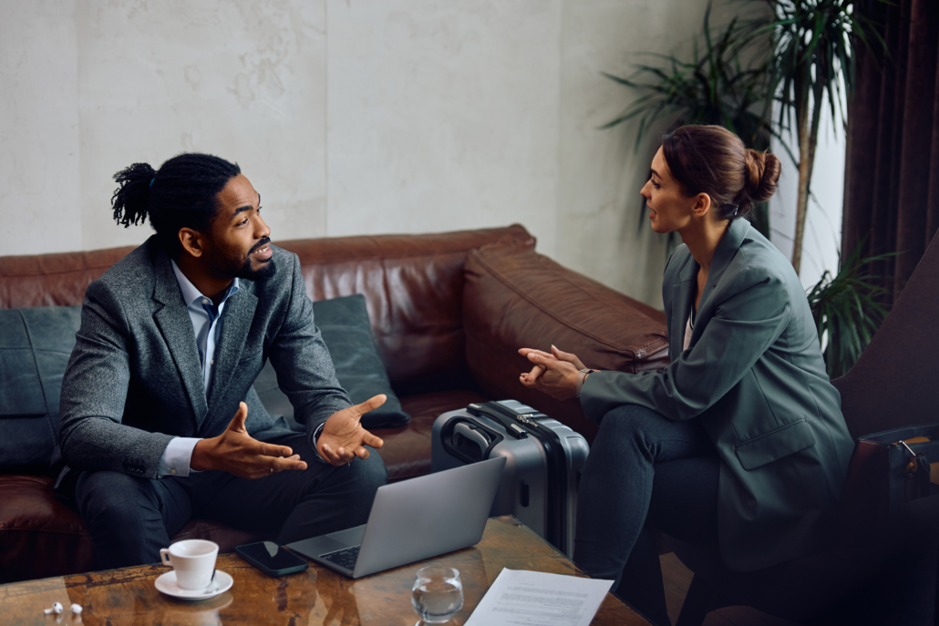 Multiracial Business Couple Talking During A Meeting In Hotel Lobby.